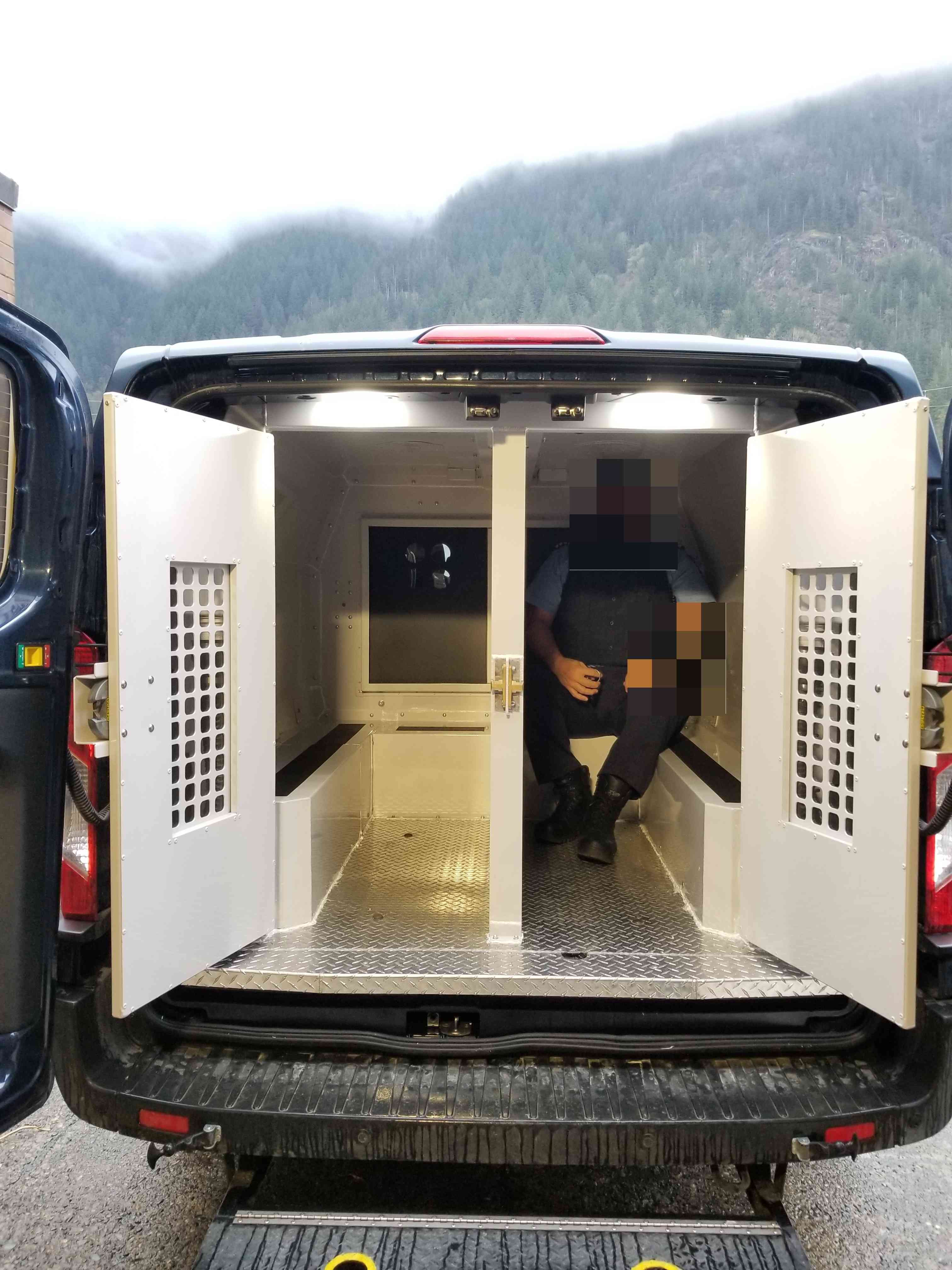 Rear photo of a CSC prisoner transport vehicle with a male guard seated inside the prisoner compartment.