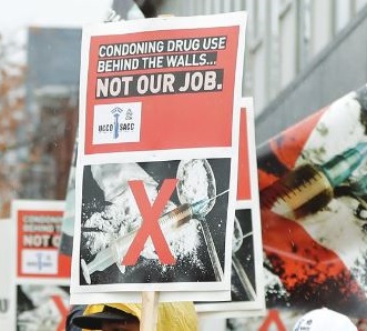 Photo of a Union of Canadian Correctional Officers (UCCO) picket sign that states: CONDONING DRUG USE BEHIND THE WALLS NOT OUR JOB.
