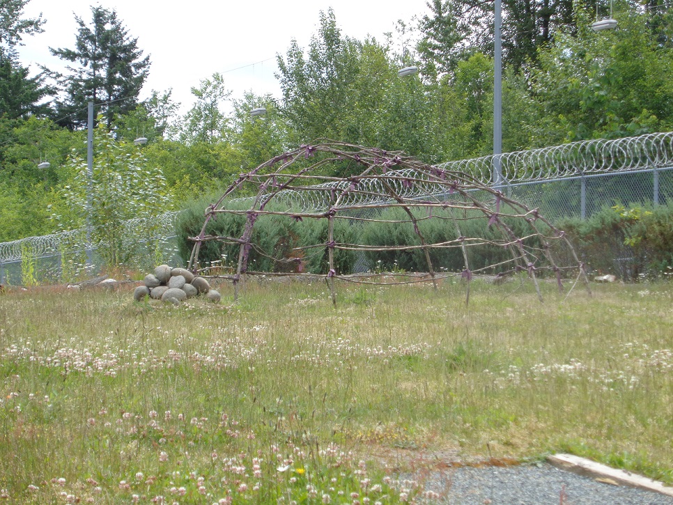 Photo of the frame for a sweat lodge and the border fence at Fraser Valley Institution.