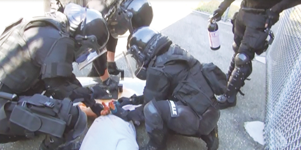 Photo of four officers from the emergency response team dressed in full protective equipment restraining an inmate.