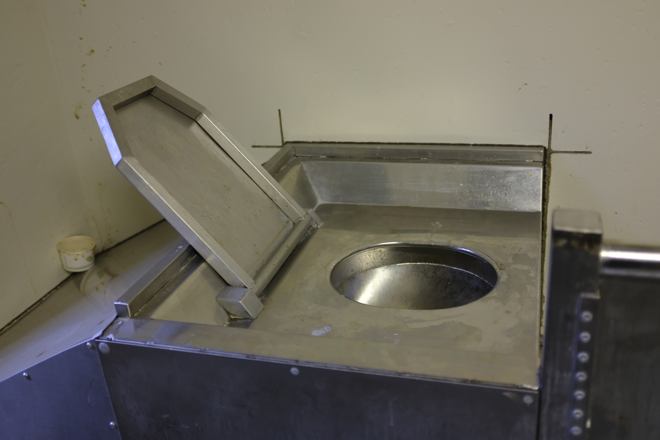 Photo of a dry cell toilet with an open seat cover at Donnacona Institution.