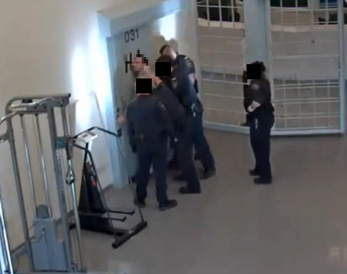 Photo d'un détenu pressé contre une porte d'acier alors qu'il est menotté