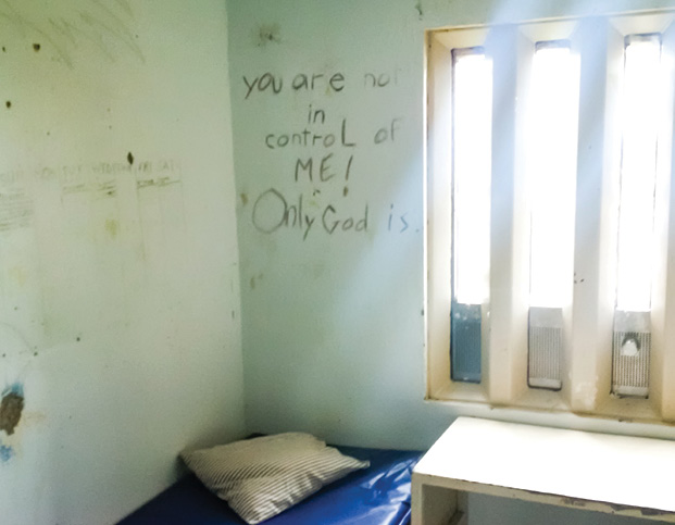 Photo d'une cellule à l'Établissement de Port Cartier comportant un graffiti sur le mur indiquant  : « Seul Dieu peut exercer un contrôle sur moi » (« you are not in control of me! Only God is. »)