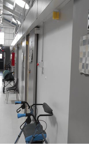 A picture of the range for older offenders at the Federal Training Centre.  The picture depicts a walker and a wheelchair in front of cell doors.