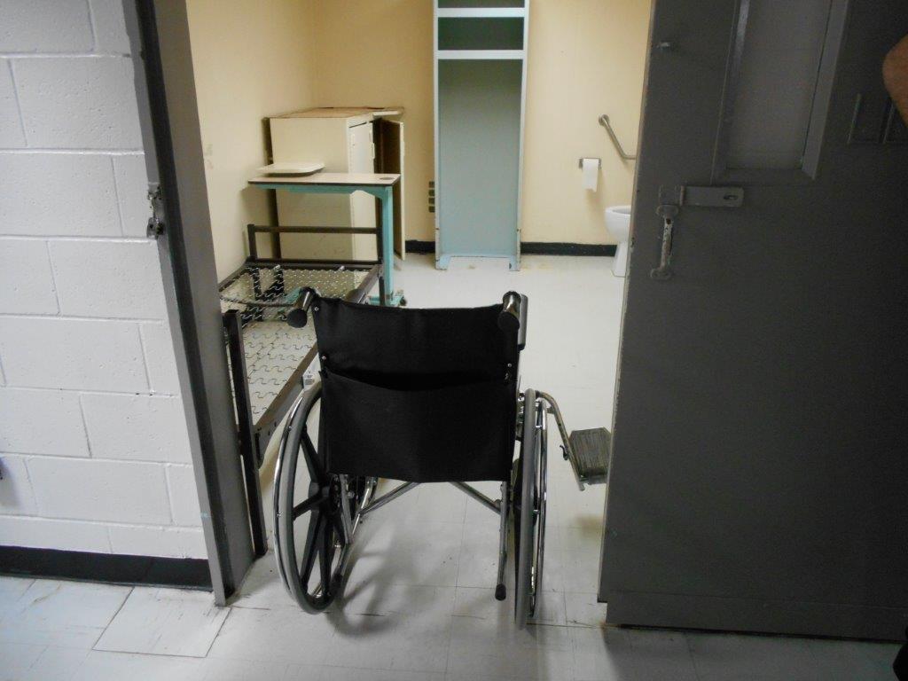 Photo d’un fauteuil roulant dans le cadre de la porte d’une cellule accessible.